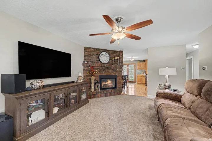 Brick fireplace, ceiling fan with light fixture, carpeted flooring, light-toned walls, and recessed lighting