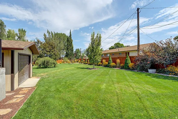 Expansive backyard featuring a lush, manicured lawn with mature landscaping including tall evergreens and flowering shrubs