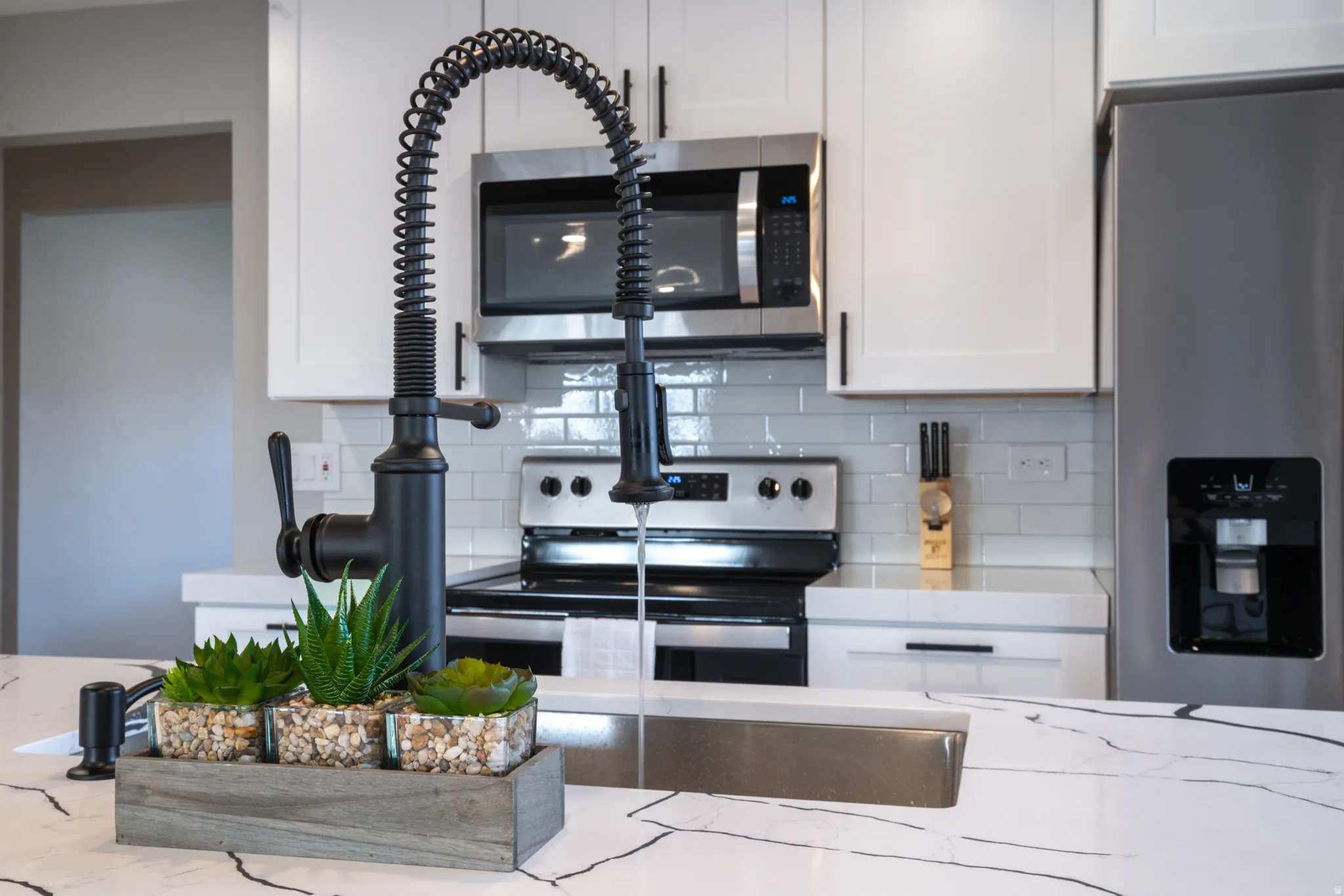 Expansive countertop with a rectangular undermount sink, matte black pull-down faucet, and white shaker-style cabinetry