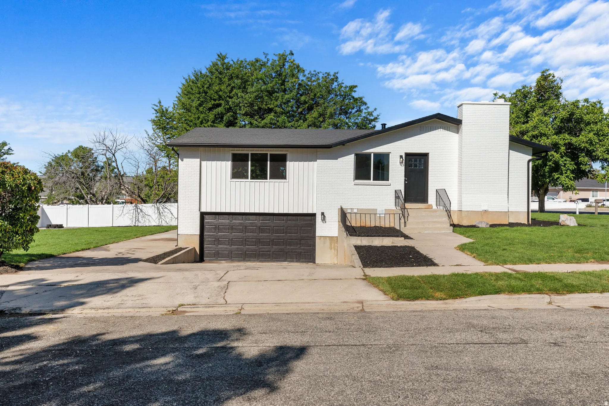 White exterior with black trim, integrated garage, concrete driveway, and front entry with steps