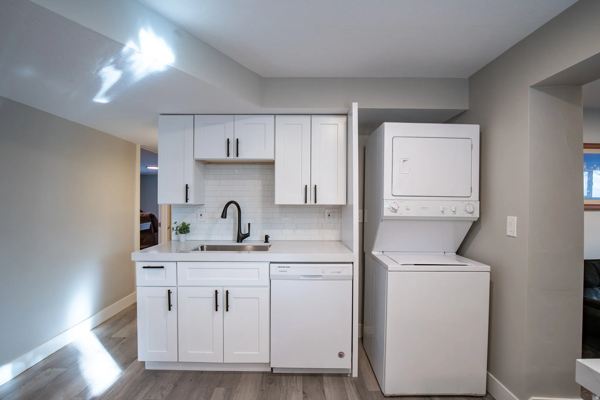 Contemporary kitchen featuring white cabinetry, a stainless steel sink with a matte black faucet, a white subway tile backsplash, and a built-in dishwasher