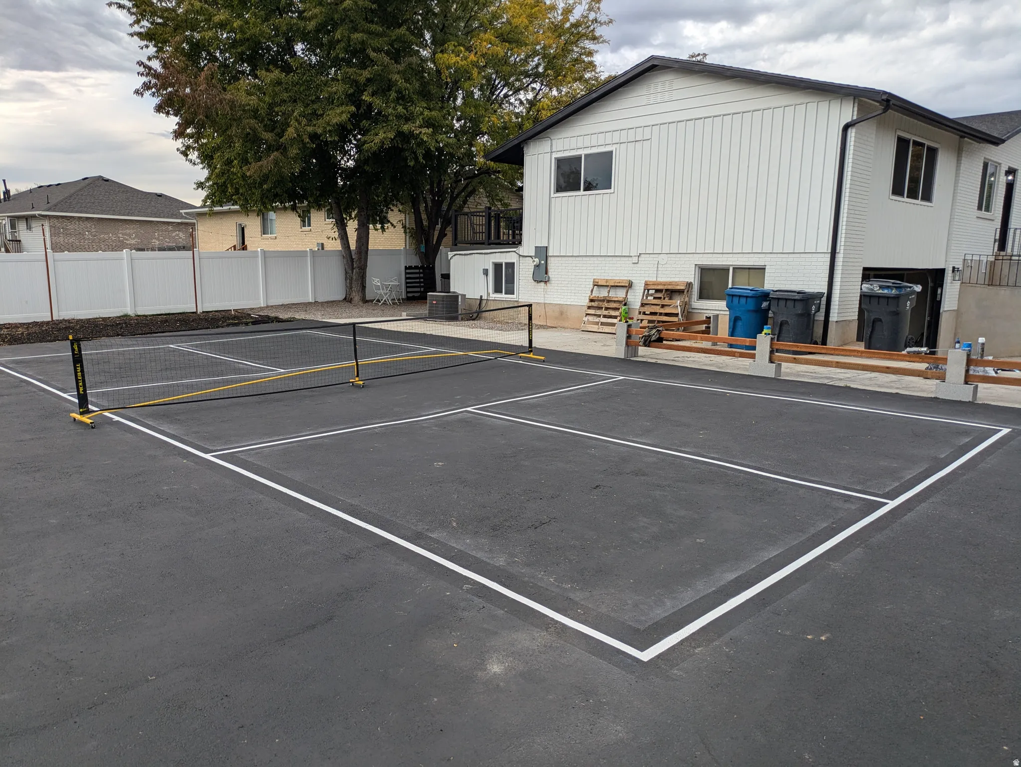 Paved court featuring white line markings and a net, situated alongside a white-sided exterior