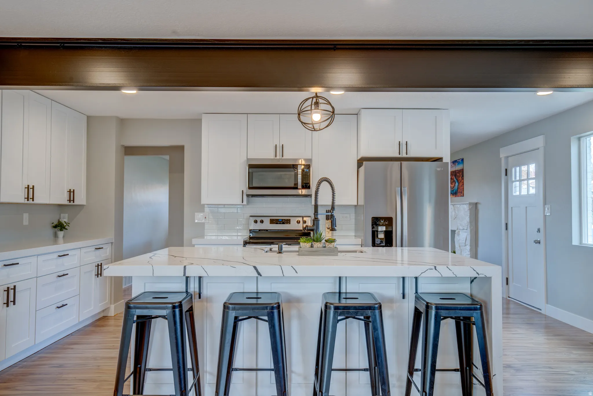 Modern kitchen featuring an extended island with a waterfall edge, stainless steel appliances, white flat-panel cabinetry, and wood-finish flooring