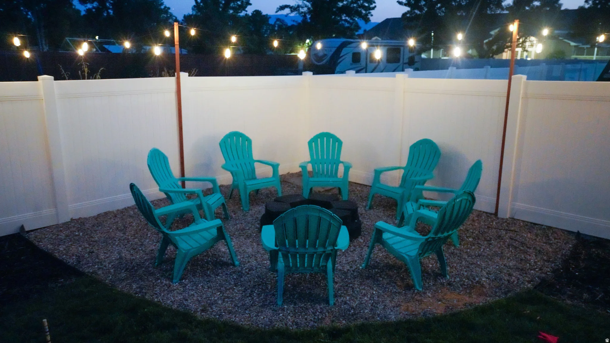 Gravel patio area featuring a white privacy fence and string lighting