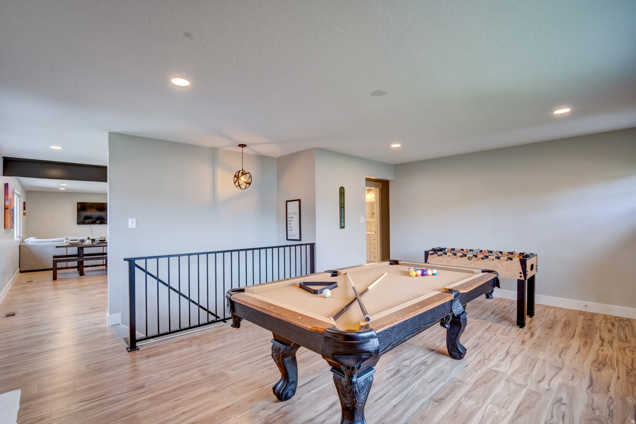 Spacious recreation room featuring wood-finish flooring, recessed lighting, and a black metal railing