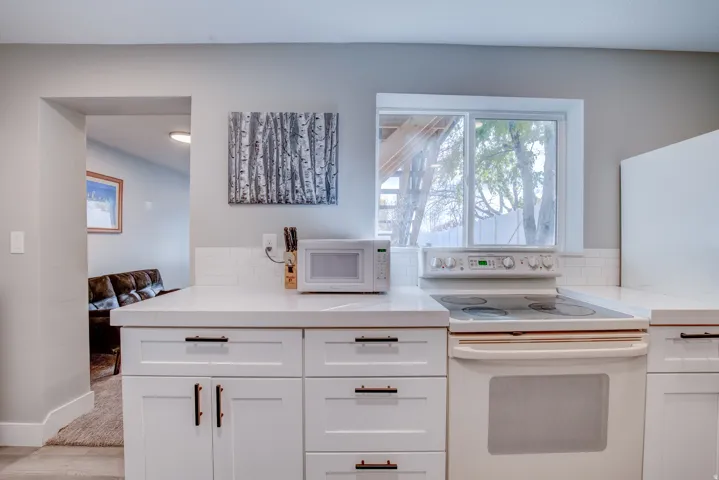 White shaker-style cabinetry with dark hardware, solid surface countertops, electric range, and a subway tile backsplash