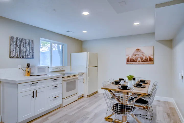 Kitchen area featuring white cabinetry, light-toned countertops, a white subway tile backsplash, and light wood-finish flooring