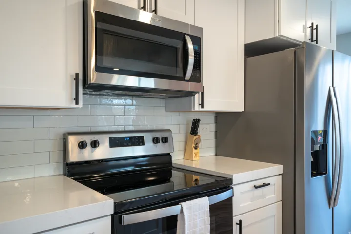 Stainless steel appliances, white cabinetry, integrated microwave, electric range, and light-toned countertops