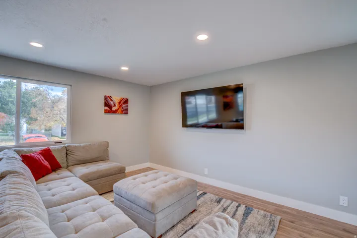 Recessed ceiling lighting, light gray wall paint, wood-finish flooring, white trim, and a large window