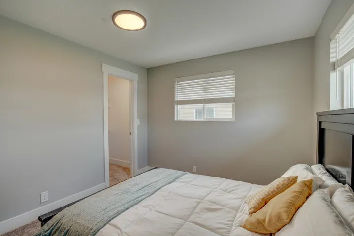 Bright secondary bedroom featuring neutral wall finishes, recessed ceiling lighting, large window with horizontal blinds providing natural light, and wall-mounted television