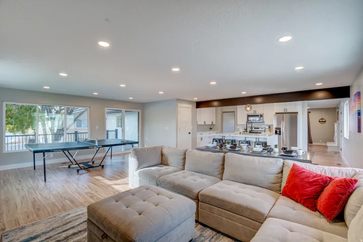 Open-concept living space with recessed lighting, wood-finish flooring, a kitchen featuring white cabinetry, a large window, and sliding glass doors