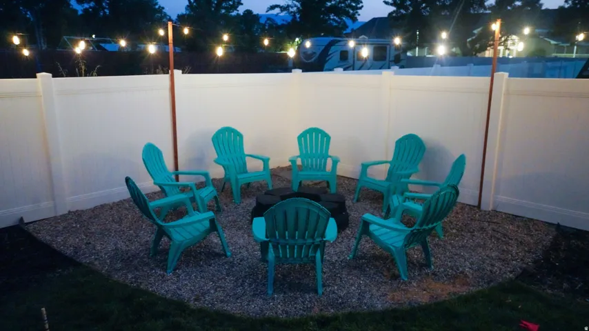 Gravel patio area featuring a white privacy fence and string lighting