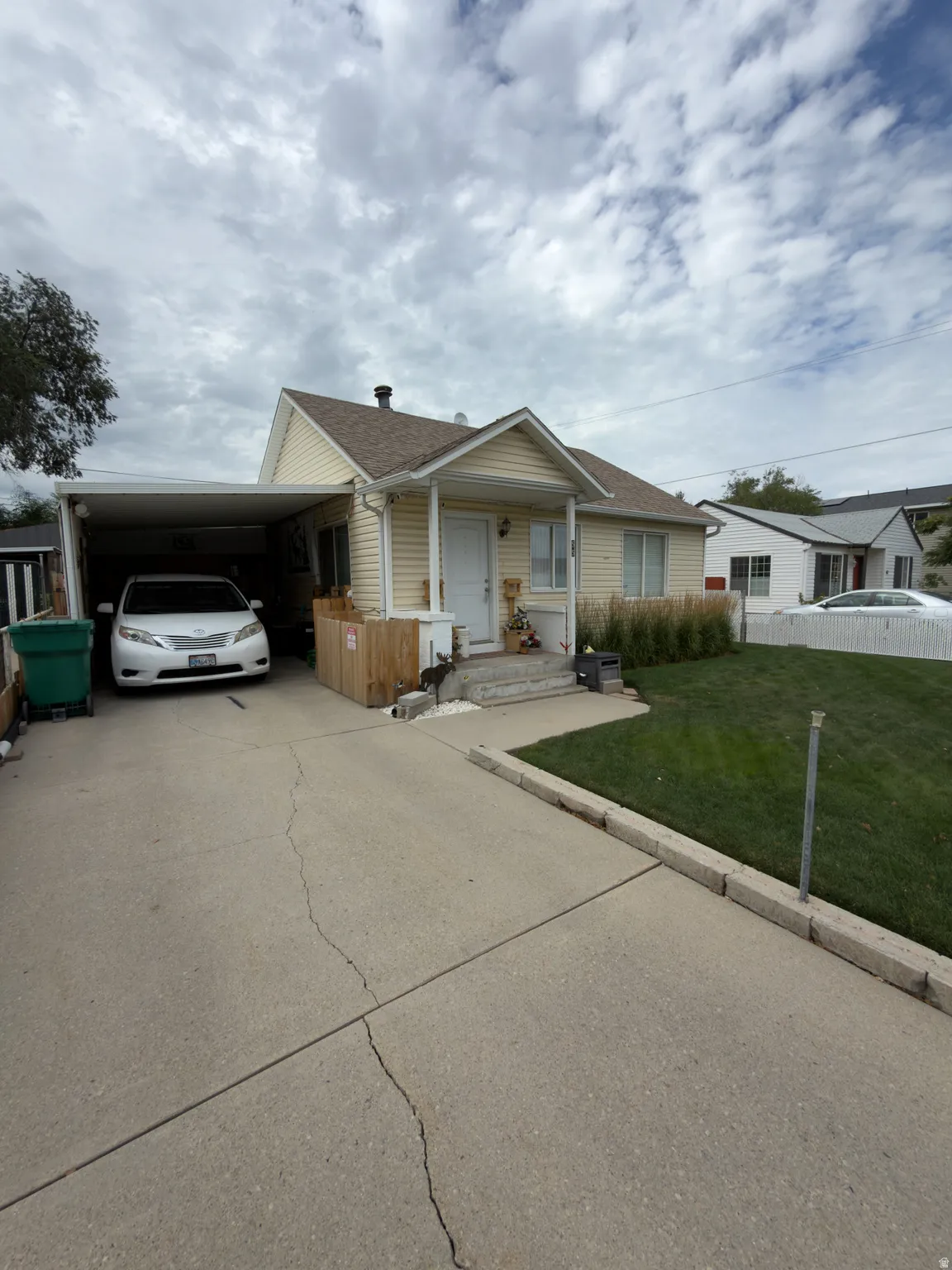Single-story residence featuring light-colored siding, a covered carport, and an established lawn