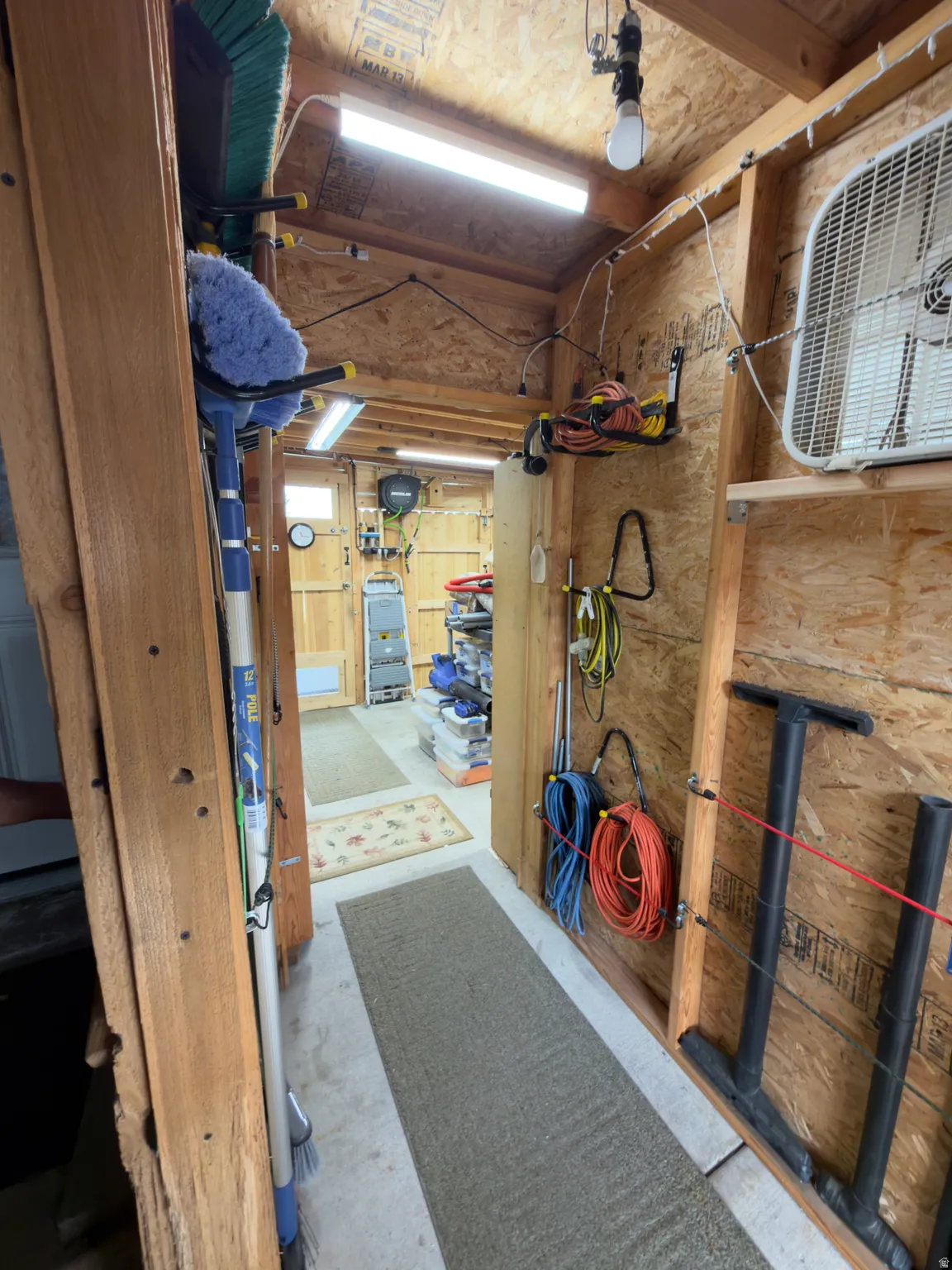Interior shed space featuring exposed wood framing, concrete flooring, and overhead lighting