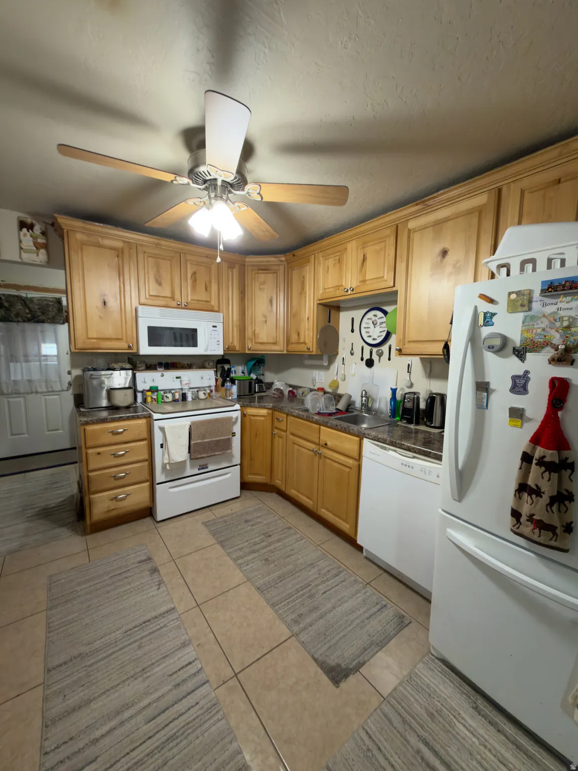 Light wood-finish cabinetry, tile flooring, and a ceiling fan with integrated lighting