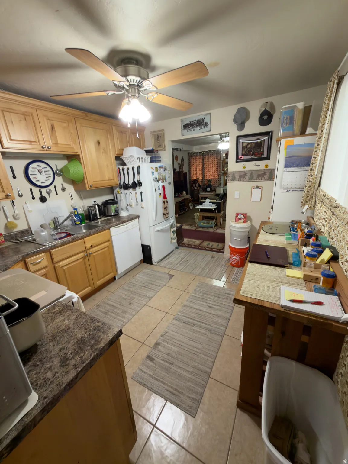 Kitchen featuring wood-finish cabinetry, a ceiling fan with integrated lighting, a built-in dishwasher, and tile flooring