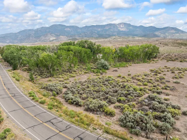 Scenic acreage featuring mature cottonwood trees, native desert landscaping, and paved road frontage with mountain backdrop