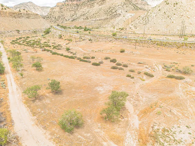 Expansive undeveloped land featuring a natural terrain, scattered trees, and a distant paved road