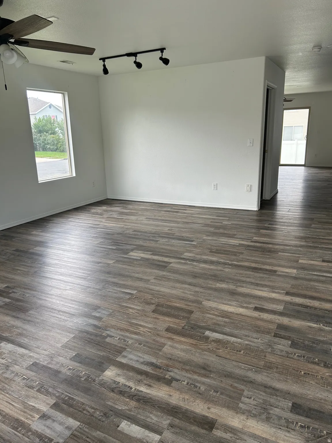 Wood-finish flooring throughout, ceiling fan with integrated lighting, track lighting fixture, and a rectangular window
