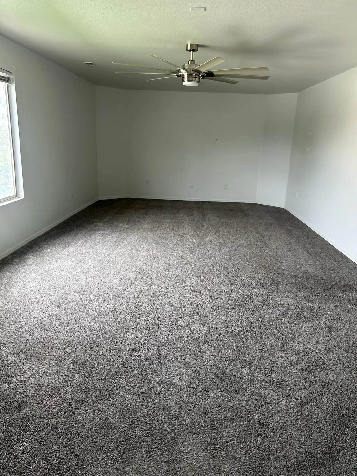 Spacious interior featuring neutral carpeting, a large window, a modern ceiling fan with lighting, and recessed ceiling lighting