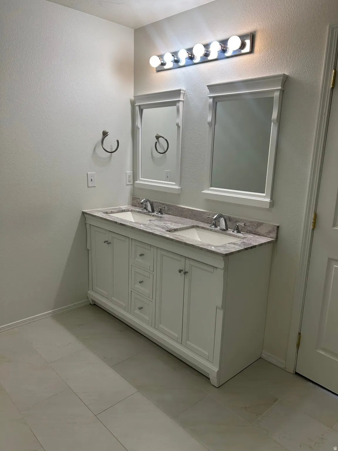 Dual vanity with granite countertop, integrated sinks, chrome fixtures, and white cabinetry