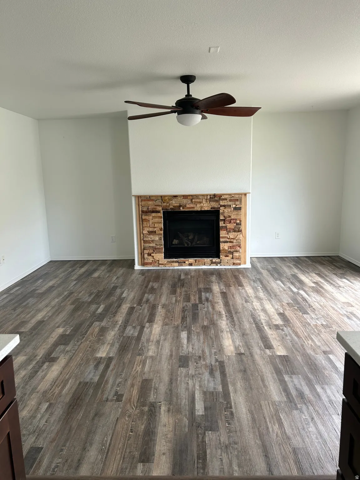 Spacious room featuring wood-finish flooring, a stone-clad fireplace, and a ceiling fan with integrated lighting