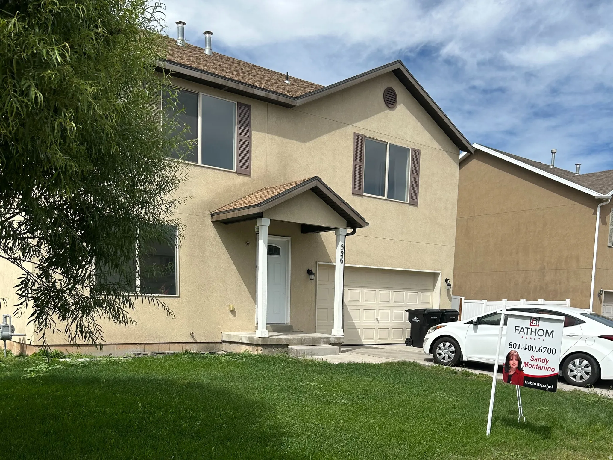 Two-story stucco exterior, covered entry with columns, attached garage, and a front lawn with mature landscaping
