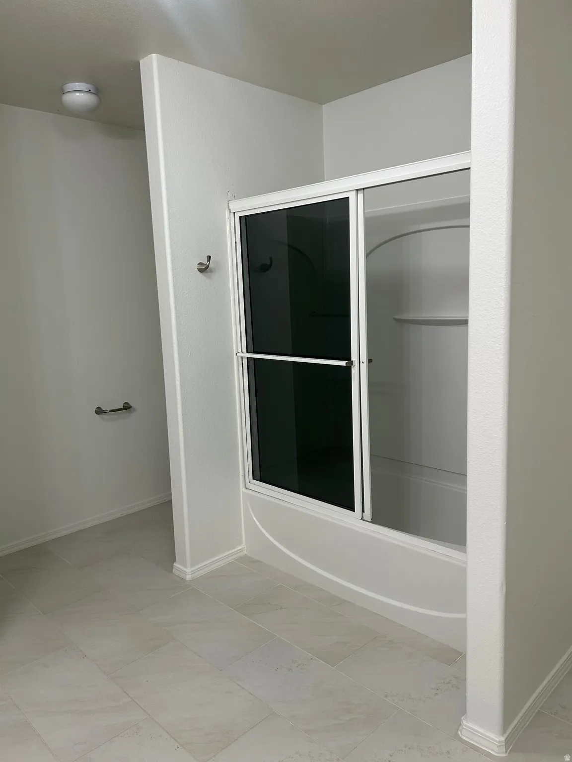 Tub-shower combination with sliding glass doors, light-toned wall tile, and a towel bar