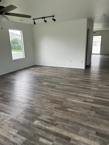 Wood-finish flooring throughout, ceiling fan with integrated lighting, track lighting fixture, and a rectangular window
