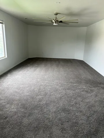 Spacious interior featuring neutral carpeting, a large window, a modern ceiling fan with lighting, and recessed ceiling lighting