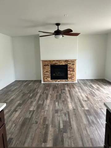 Spacious room featuring wood-finish flooring, a stone-clad fireplace, and a ceiling fan with integrated lighting