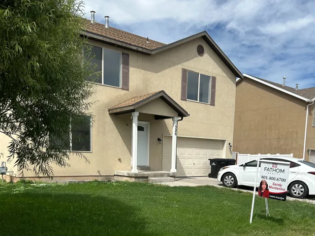 Two-story stucco exterior, covered entry with columns, attached garage, and a front lawn with mature landscaping