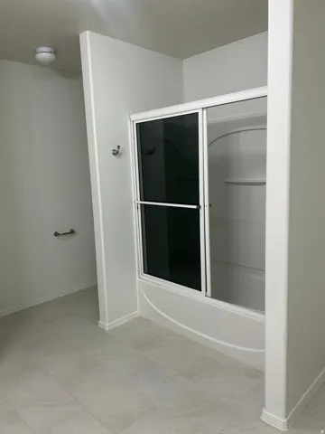 Tub-shower combination with sliding glass doors, light-toned wall tile, and a towel bar