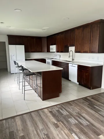 Kitchen featuring dark wood cabinetry, light countertops, white tile flooring, stainless steel appliances, and a central island with seating