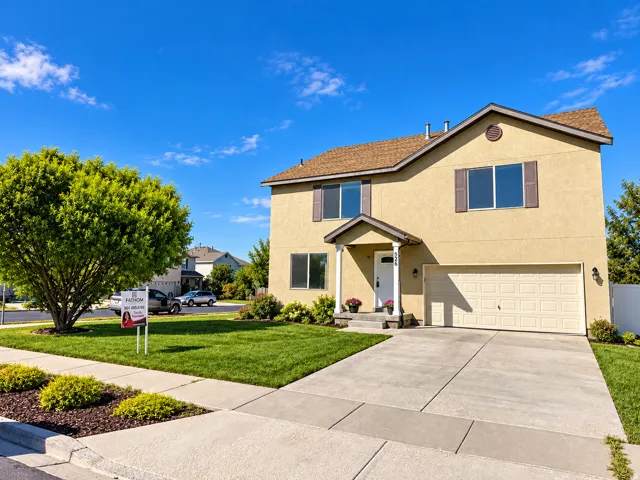 Stucco exterior with a covered porch entrance, attached garage, concrete driveway, and a large front lawn