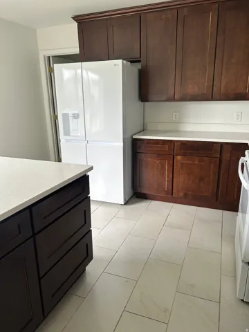 Dark wood cabinetry, light-toned countertops, large format tile flooring, and integrated white appliances