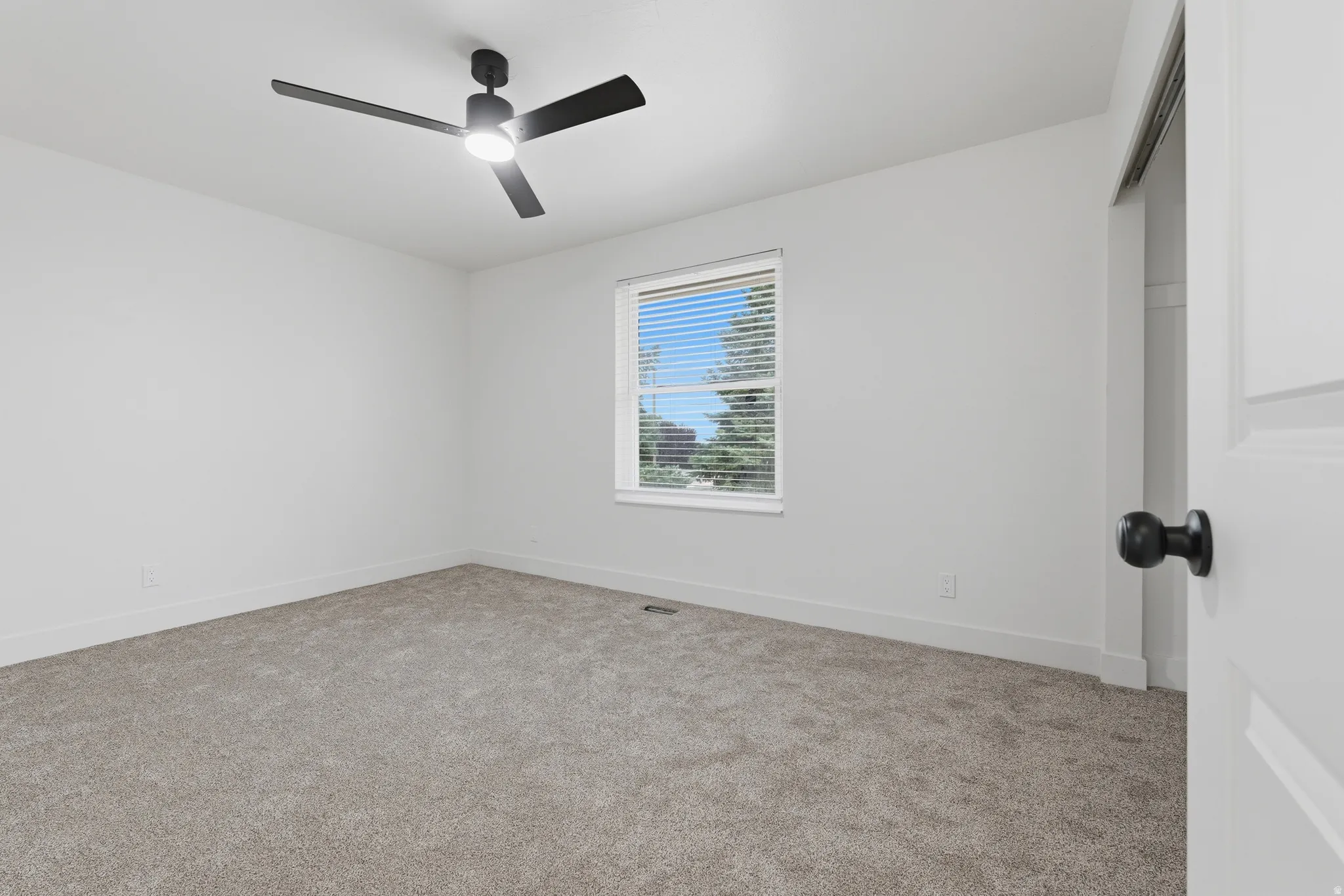 Neutral tone wall finish, textured carpeting, contemporary ceiling fan with integrated lighting, and a window with blinds