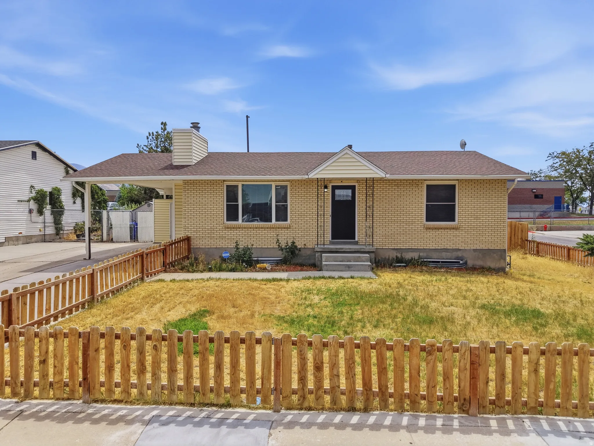 Brick exterior, covered carport, picket fencing, and a dark entry door