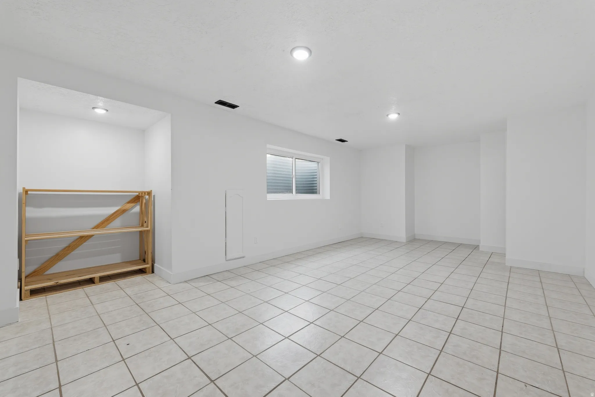 Expansive interior space with tiled flooring, recessed lighting, and a single window with horizontal blinds