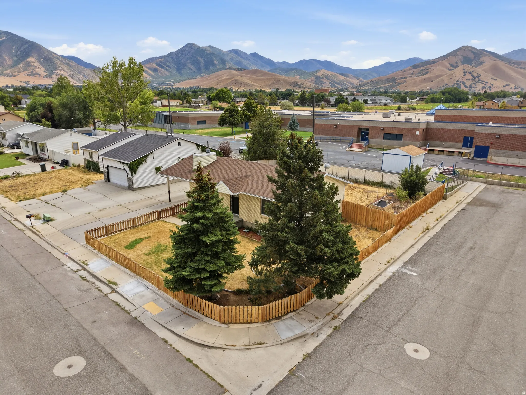 Corner lot property featuring a light-colored exterior, brown shingle roofing, and a wooden fence