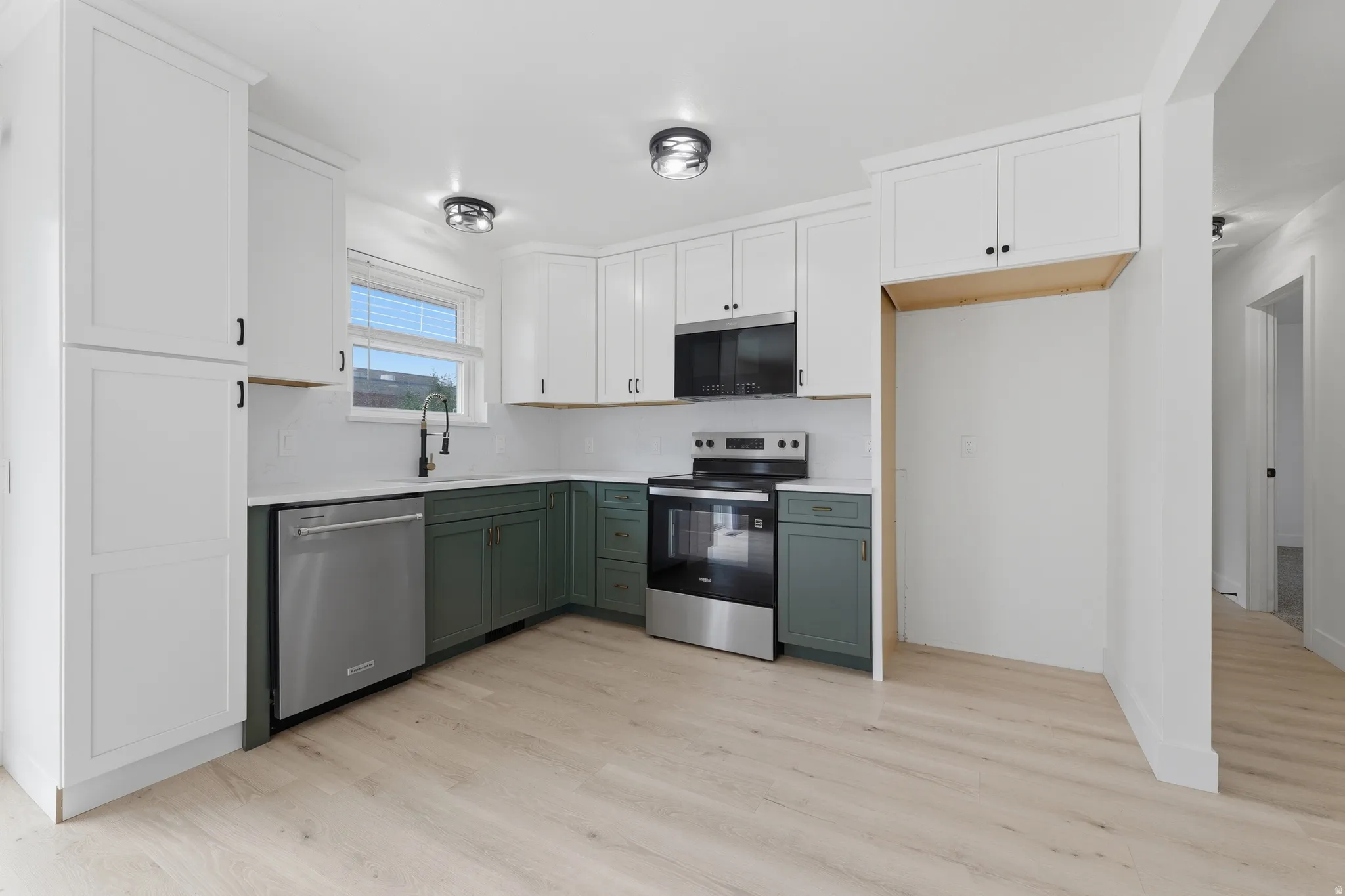 Kitchen featuring two-tone cabinetry, stainless steel appliances, light wood-finish flooring, white backsplash, and recessed lighting