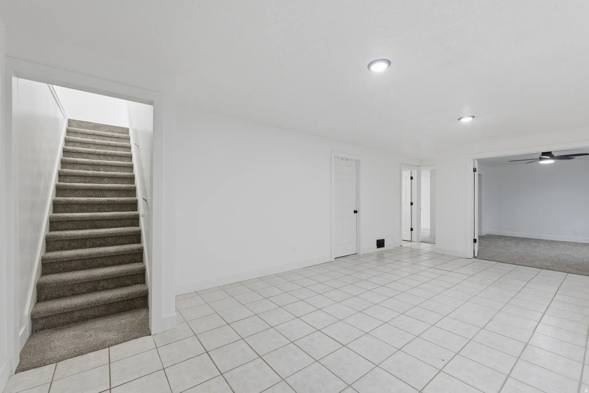 Tiled flooring in a neutral tone, recessed ceiling lighting, staircase with carpeted treads, and multiple doorways