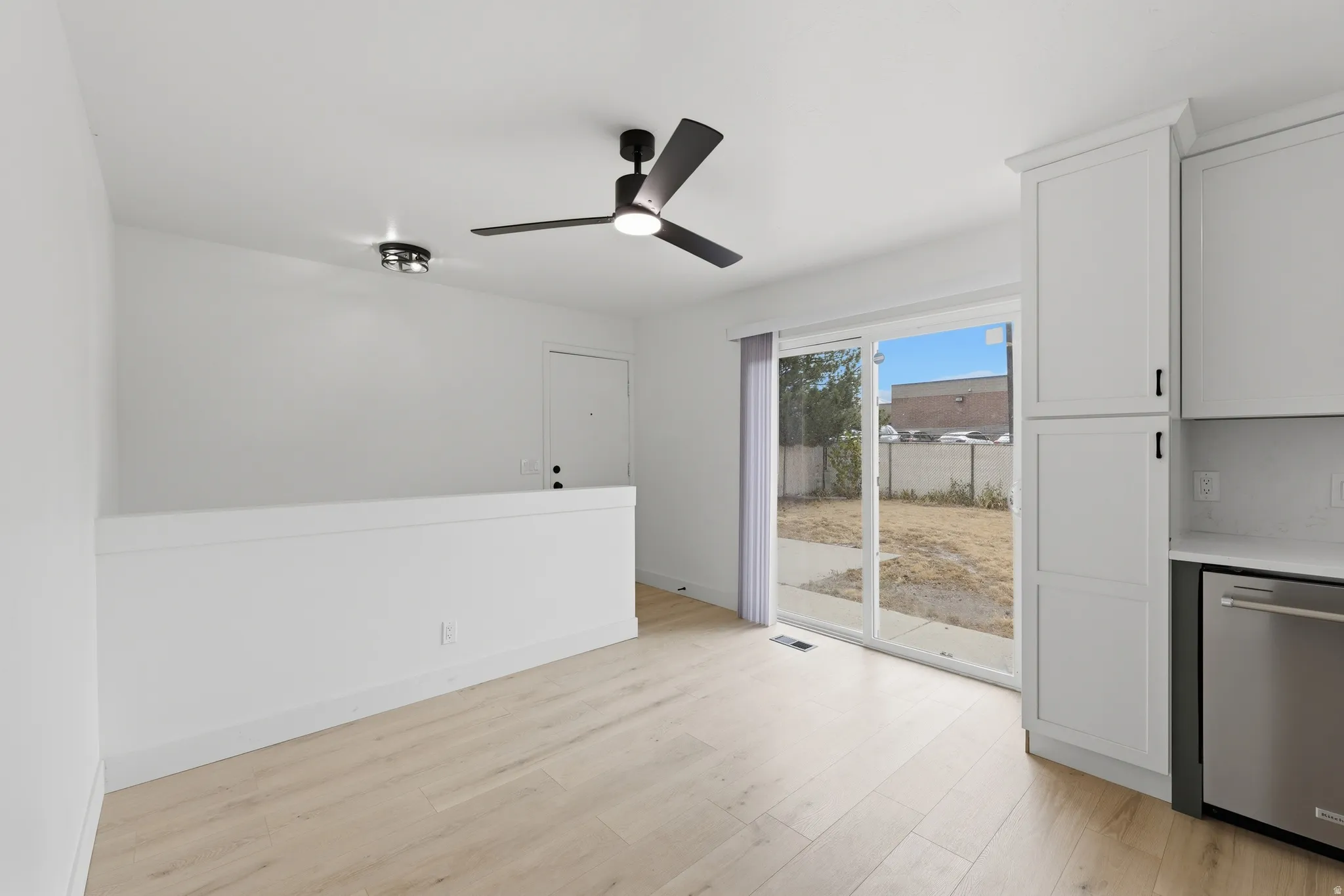 Light wood-finish flooring, white walls, and a black ceiling fan with integrated lighting