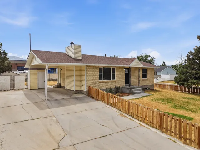 Brick and siding exterior with a covered carport, wood picket fence, and concrete driveway