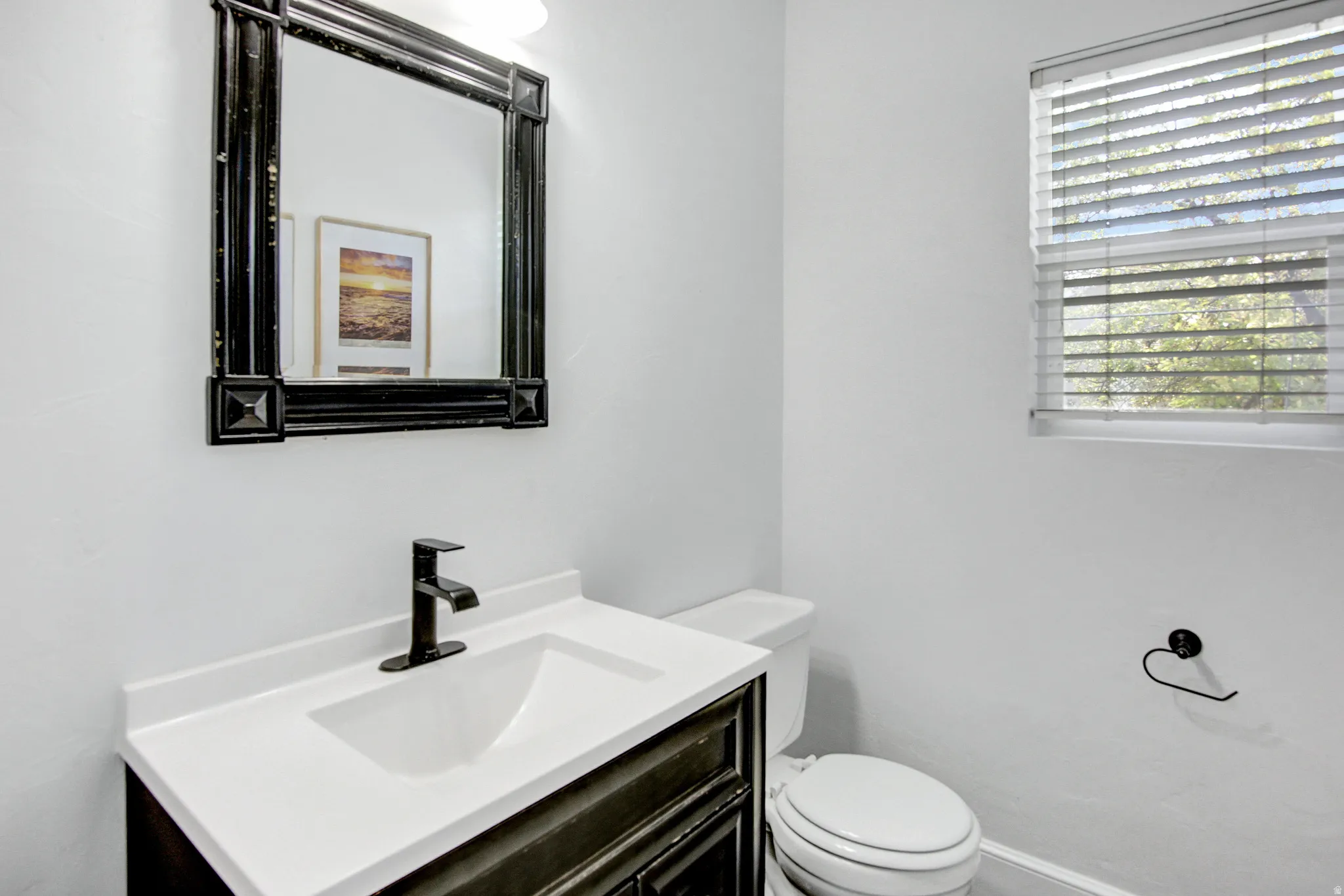 Black framed mirror over a white vanity with an integrated sink and black faucet