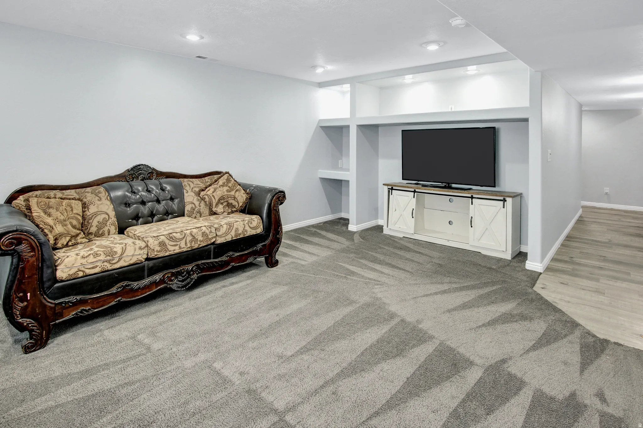 Recessed lighting throughout, gray patterned carpet, built-in shelving, white baseboards, and wood-finish flooring