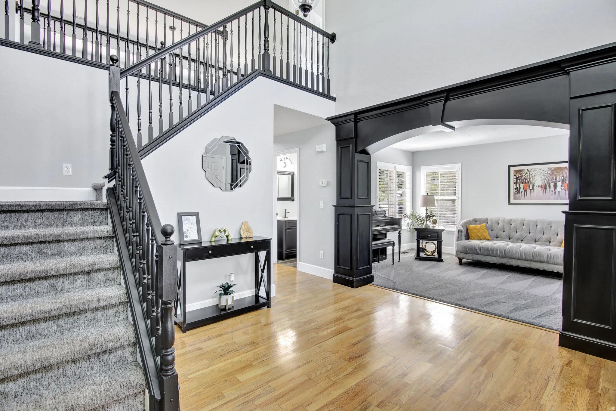 Grand two-story foyer featuring wood-finish flooring, a carpeted staircase with dark wood-finish banister, and an arched entry to an additional living space