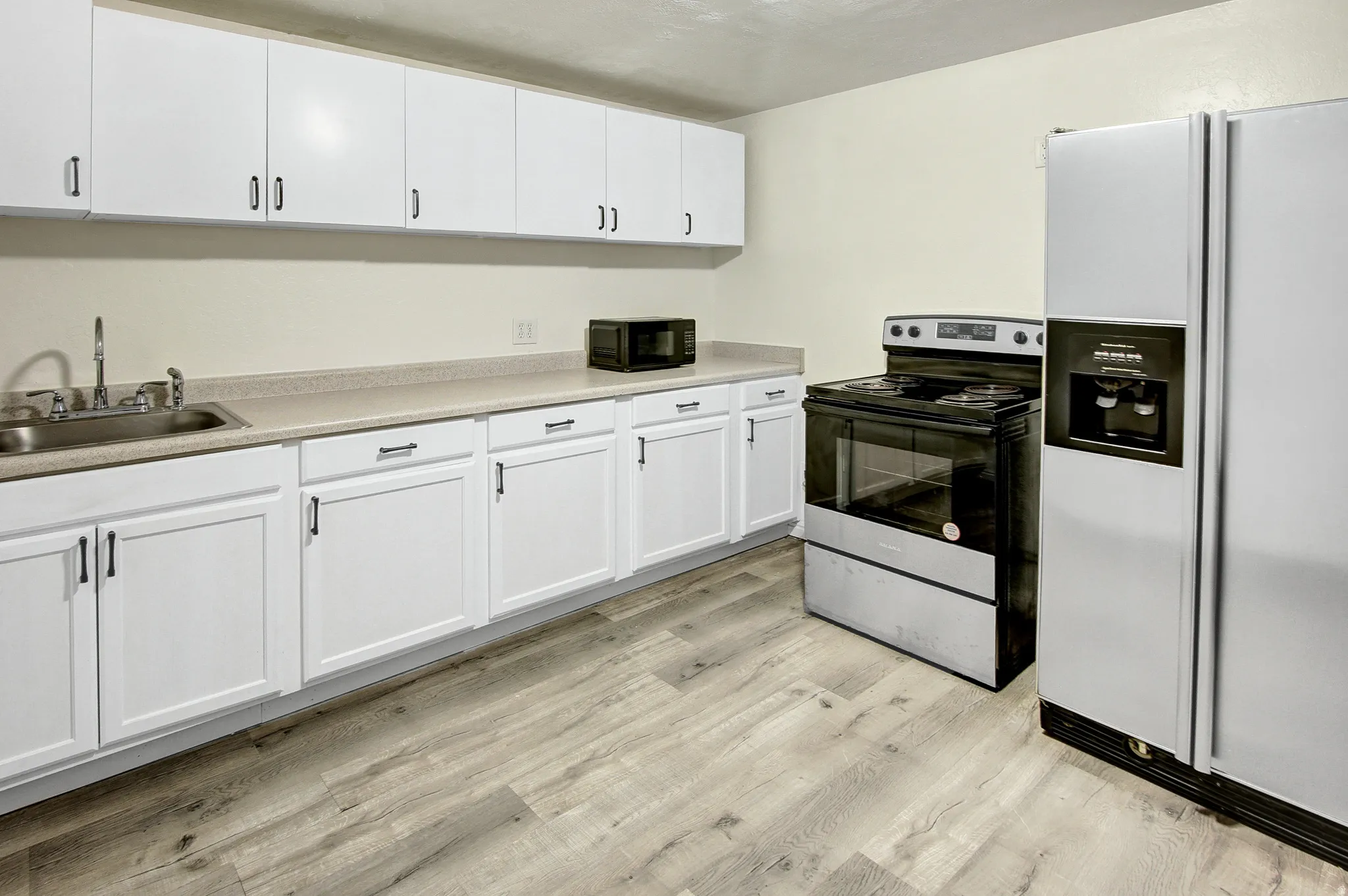Updated kitchen featuring white shaker-style cabinetry, wood-finish flooring, a stainless steel sink, and light-toned countertops