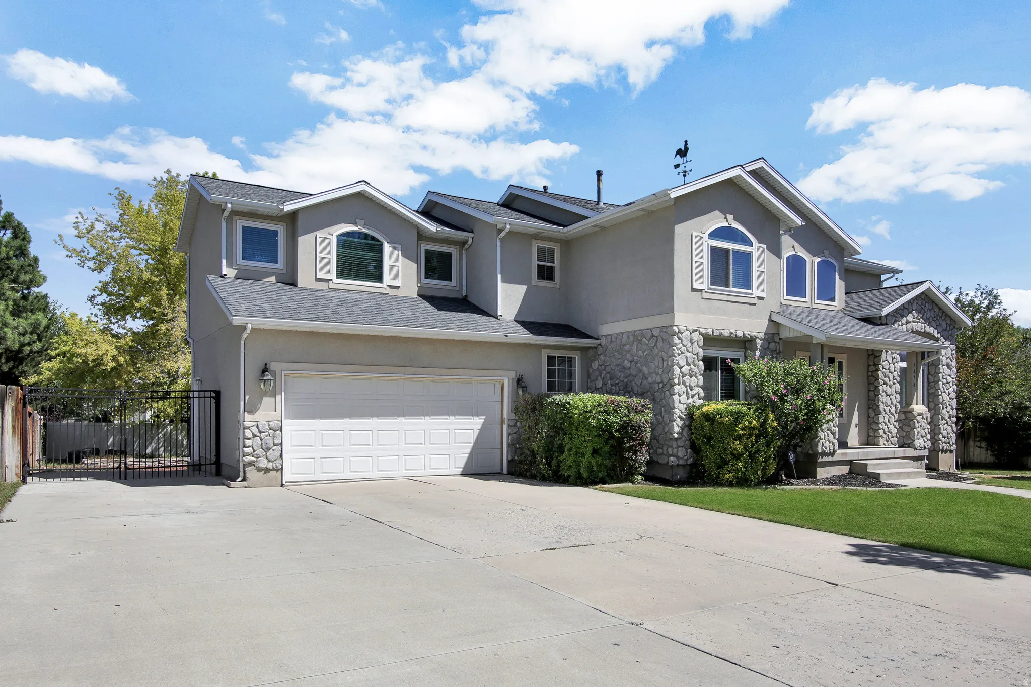 Two-story stucco residence featuring stone accents, a multi-car driveway, attached garage, and a gated side yard