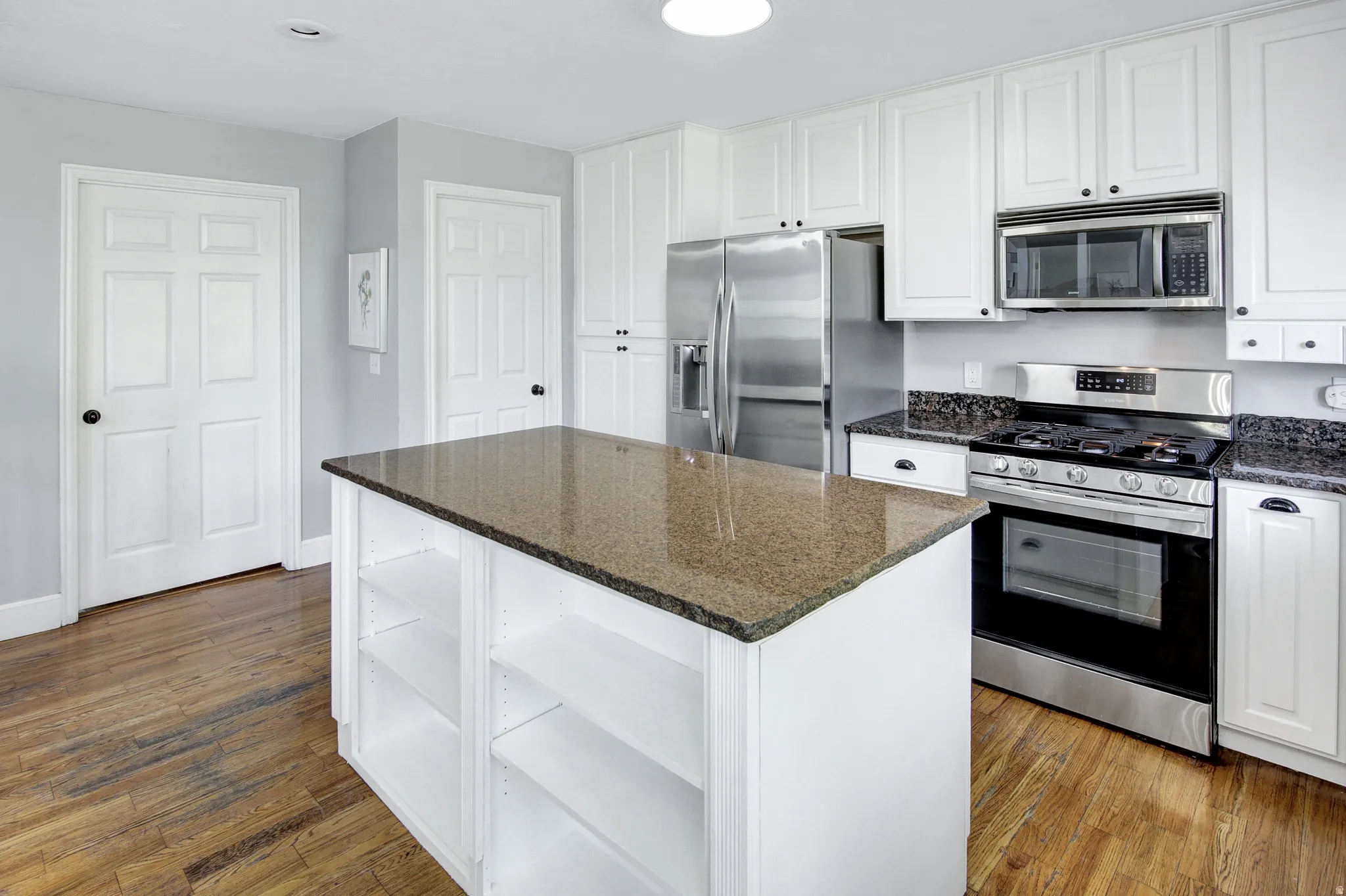 Kitchen featuring a central island with stone countertop, white cabinetry with dark hardware, stainless steel appliances, and wood-finish flooring